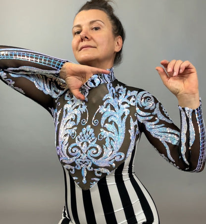 A woman poses confidently in the Glamorous sequins Stripes Catsuit costume, featuring sheer fabric, bold black-and-white stripes, blue designs, and a striking sequined leaf accent.