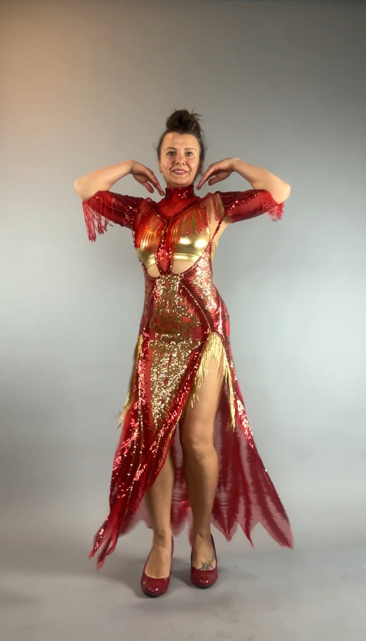 Woman wearing the bearded French accessories Sequin Sheer Dress—backless with beaded fringe—poses with arms raised against a plain gray background.
