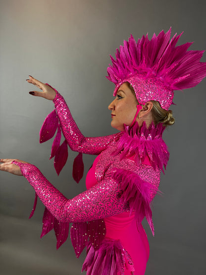 A person in profile wears the Pink bird full costume for aerial and dancers, featuring bright pink feathers and sequins, striking a dramatic pose with raised arms.