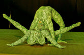Two contortionists in Green pixel Cobra Costume snake print catsuits pose in an intricate, flexible formation on stage, showcasing the custom-made Serpent Cosplay dance unitard and headdress.