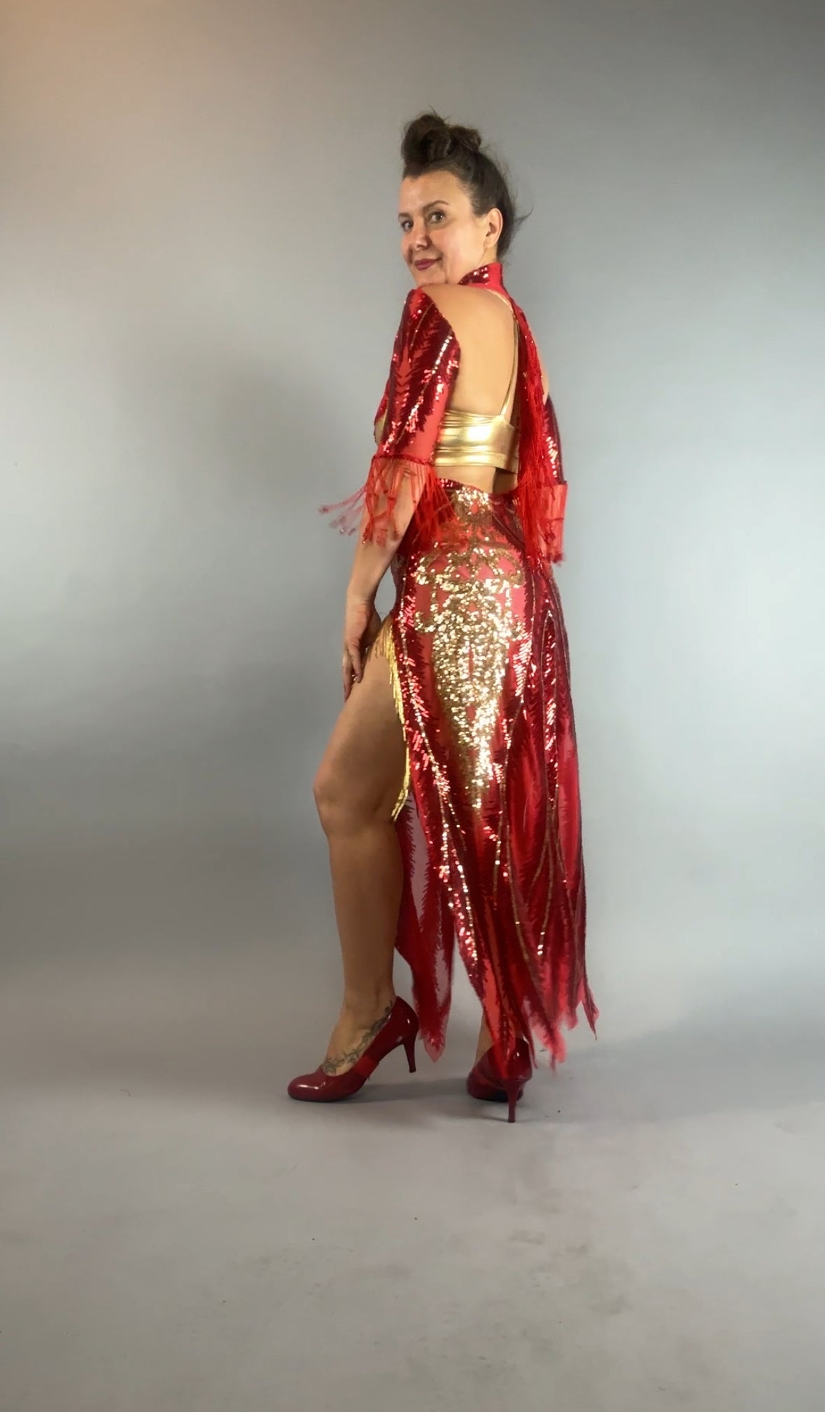 Model wears the bearded French accessories Sequin Sheer Dress featuring a backless design and beaded fringe, posing against a plain gray background.