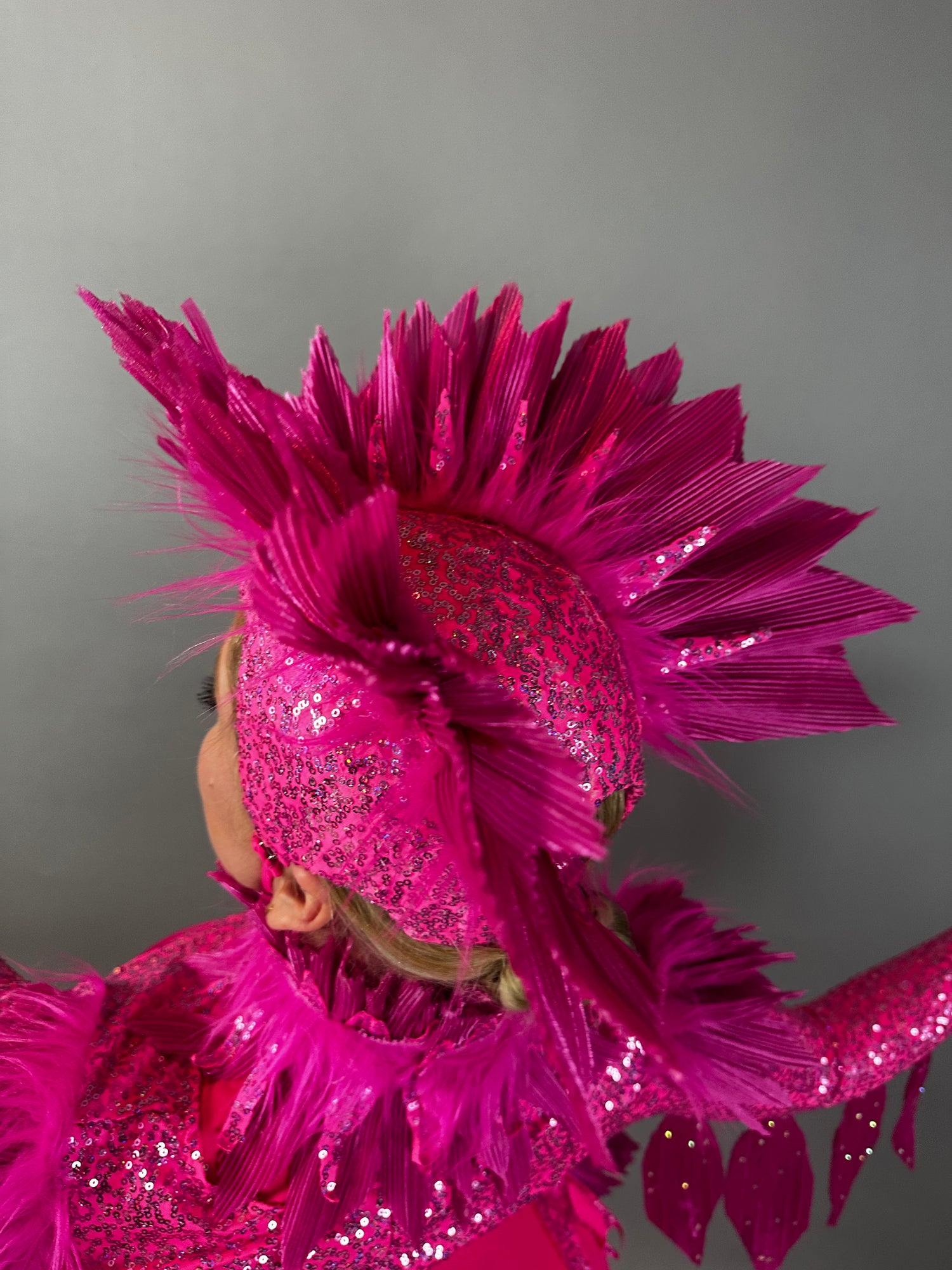 A person wears the Pink bird full costume for aerial and dancers, featuring a bright pink, glittery look with a feathered headpiece and raised arm, set against a plain background.