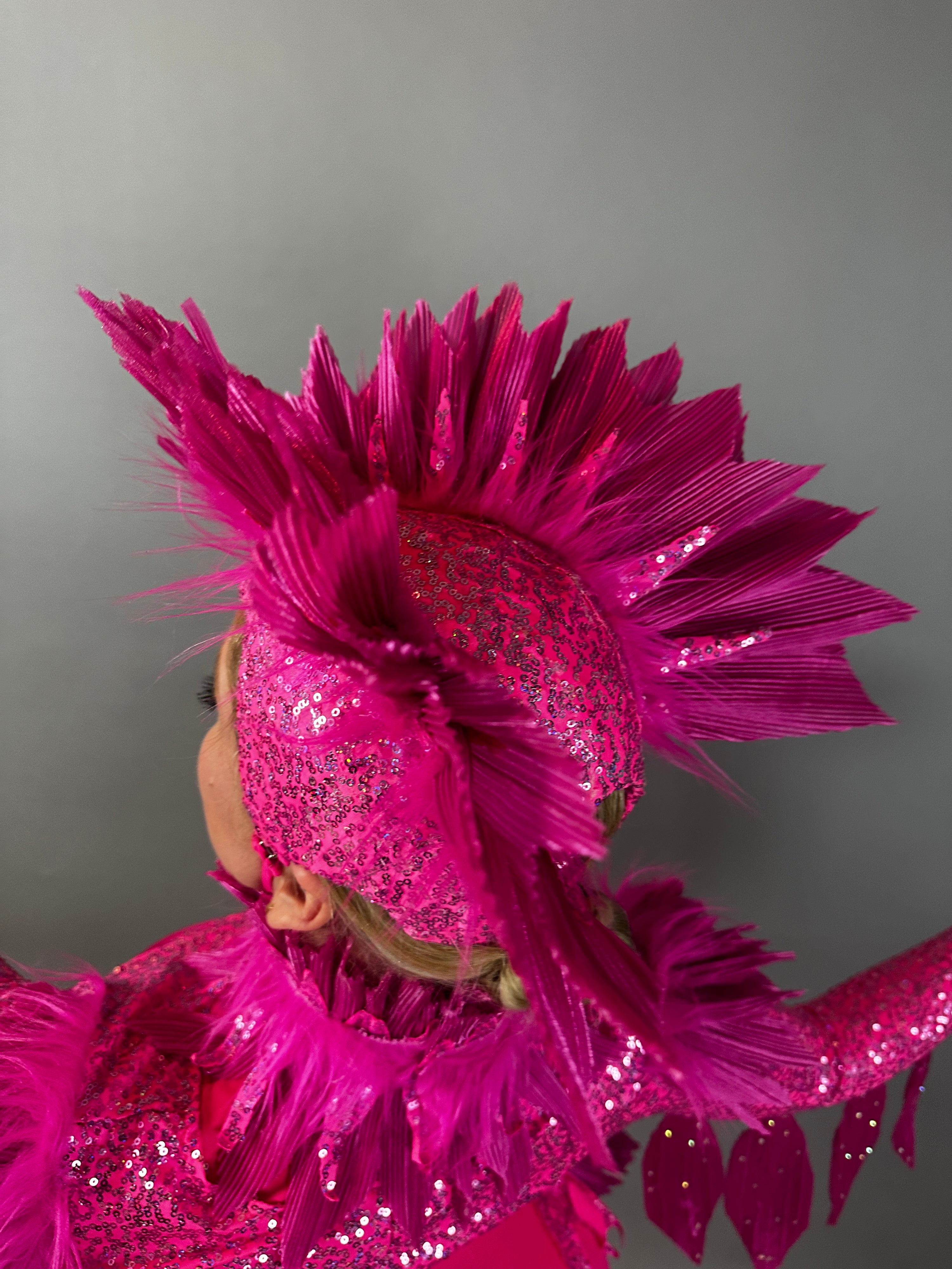 A person wears the Pink bird full costume for aerial and dancers, featuring a bright pink, glittery look with a feathered headpiece and raised arm, set against a plain background.