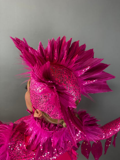 A person wears the Pink bird full costume for aerial and dancers, featuring a bright pink, glittery look with a feathered headpiece and raised arm, set against a plain background.