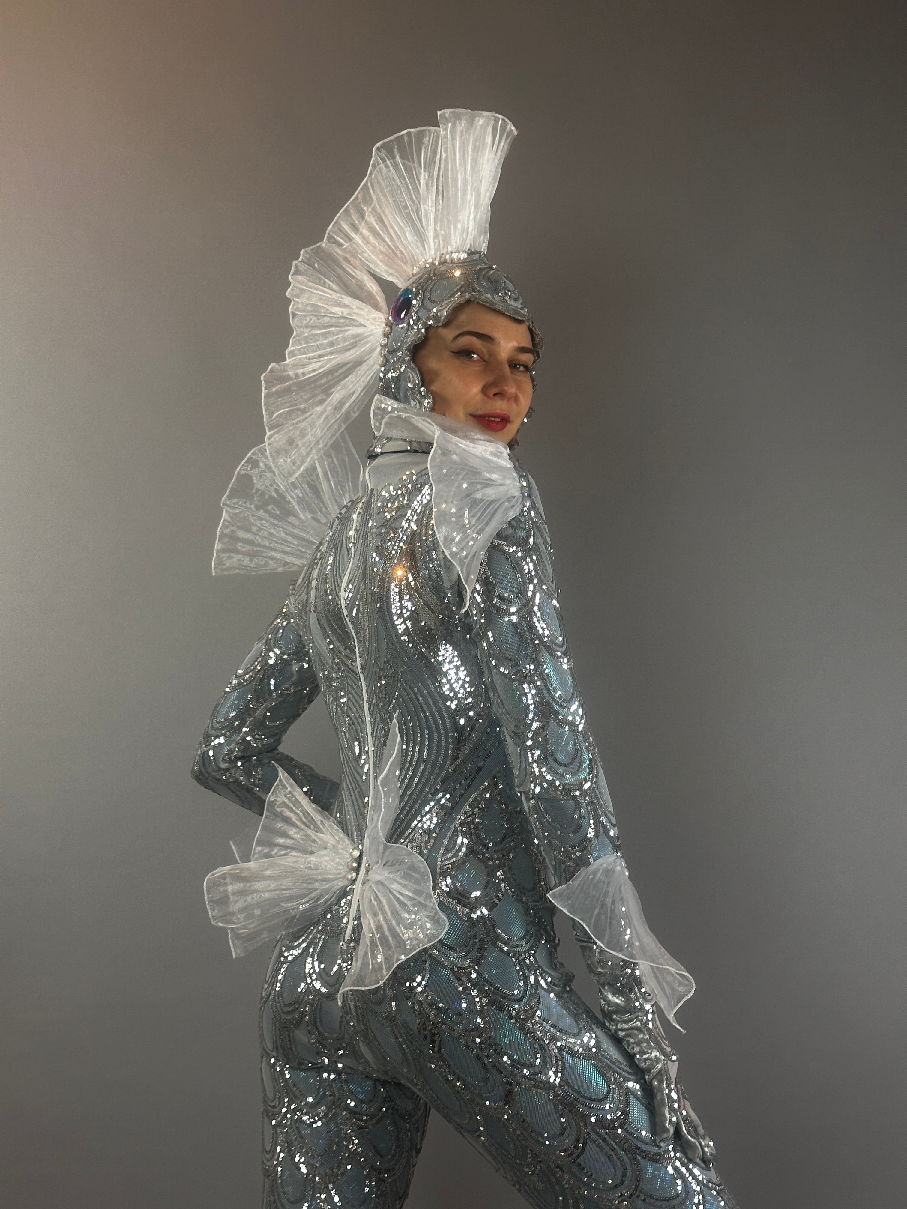 A person models the Sea Creature costume—sparkly silver with sheer fins—against a plain gray background, showcasing striking couture design.