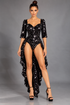 A woman in a black sequin leotard featuring a back cutout and short sleeves, styled as showgirl competition wear, poses confidently in heels against a gray backdrop.