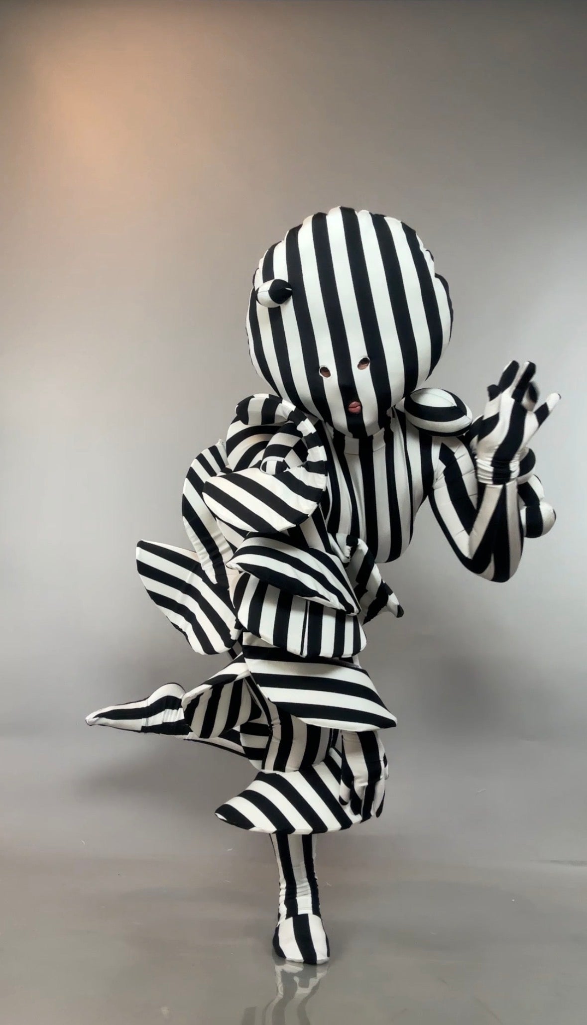 A person wearing a Black and White Striped Creature Costume with Sculptural Details in large, ruffled layers.