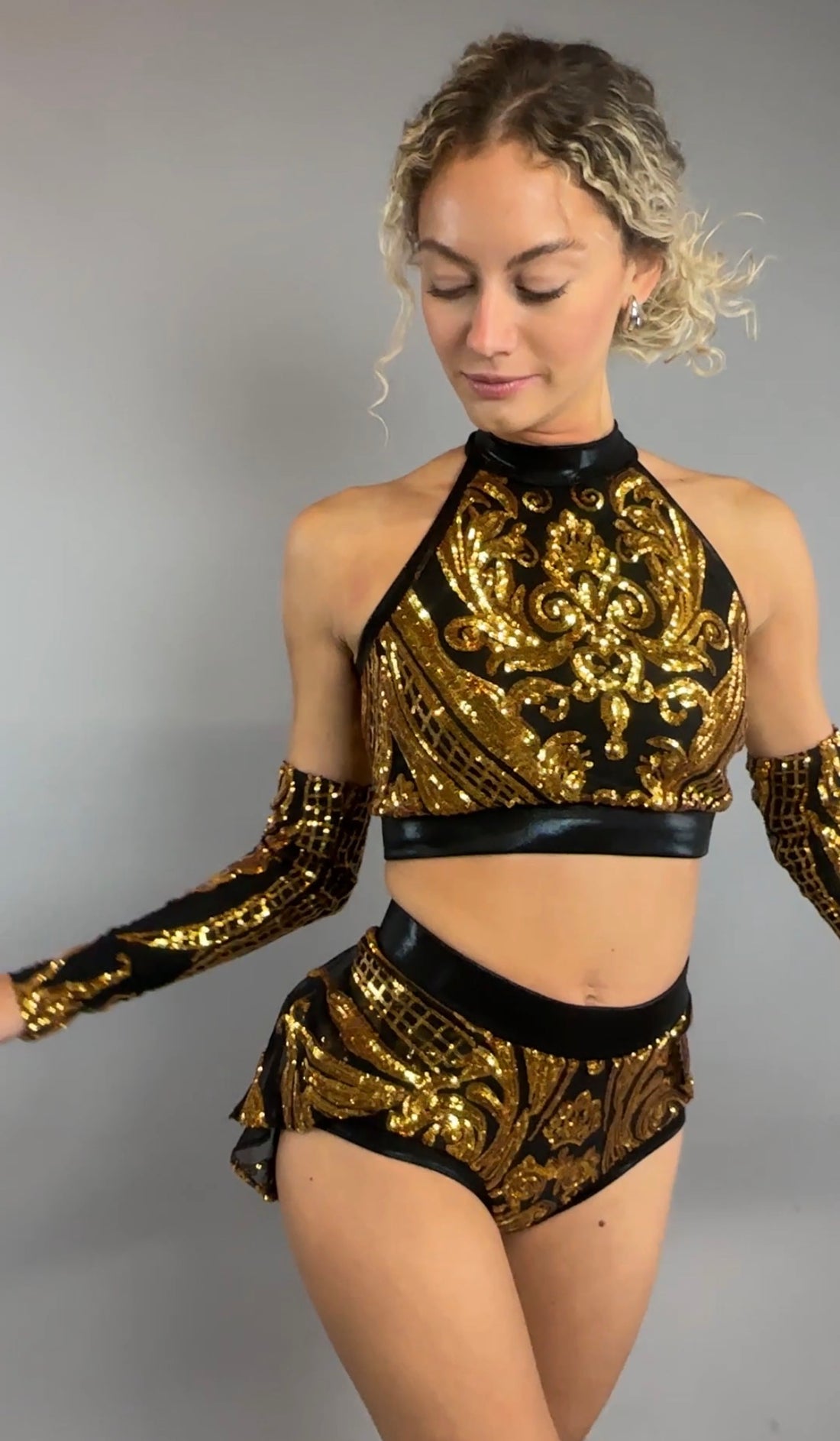A woman poses against a plain gray background wearing the Gold Sequin on Black Crop Top and Bottom Set, featuring a halterneck top with hand accessories.