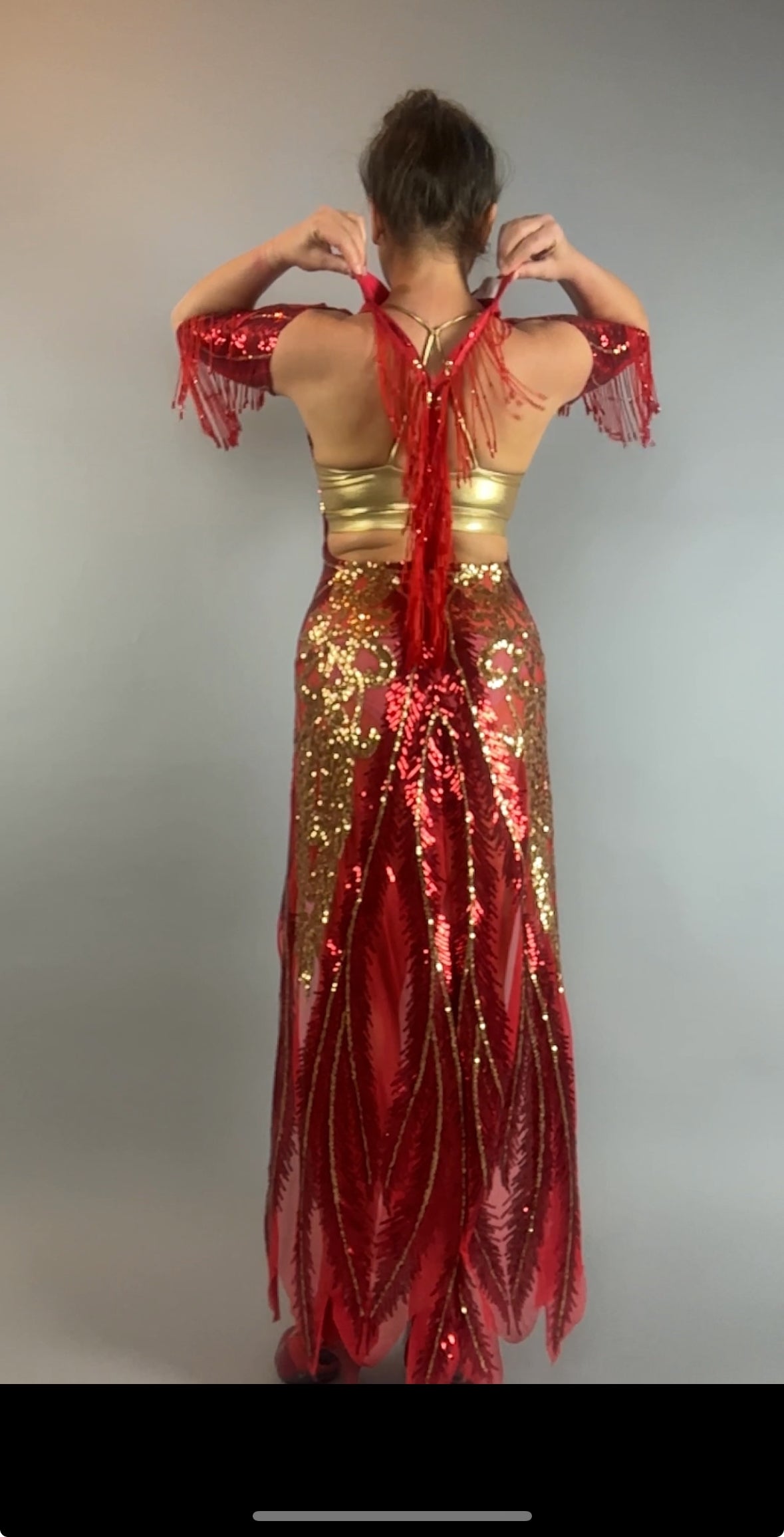 Person in a bearded French accessories Sequin Sheer Dress with beaded fringe, backless, gold and red sequins, posing with hands in a heart shape, back to the camera.