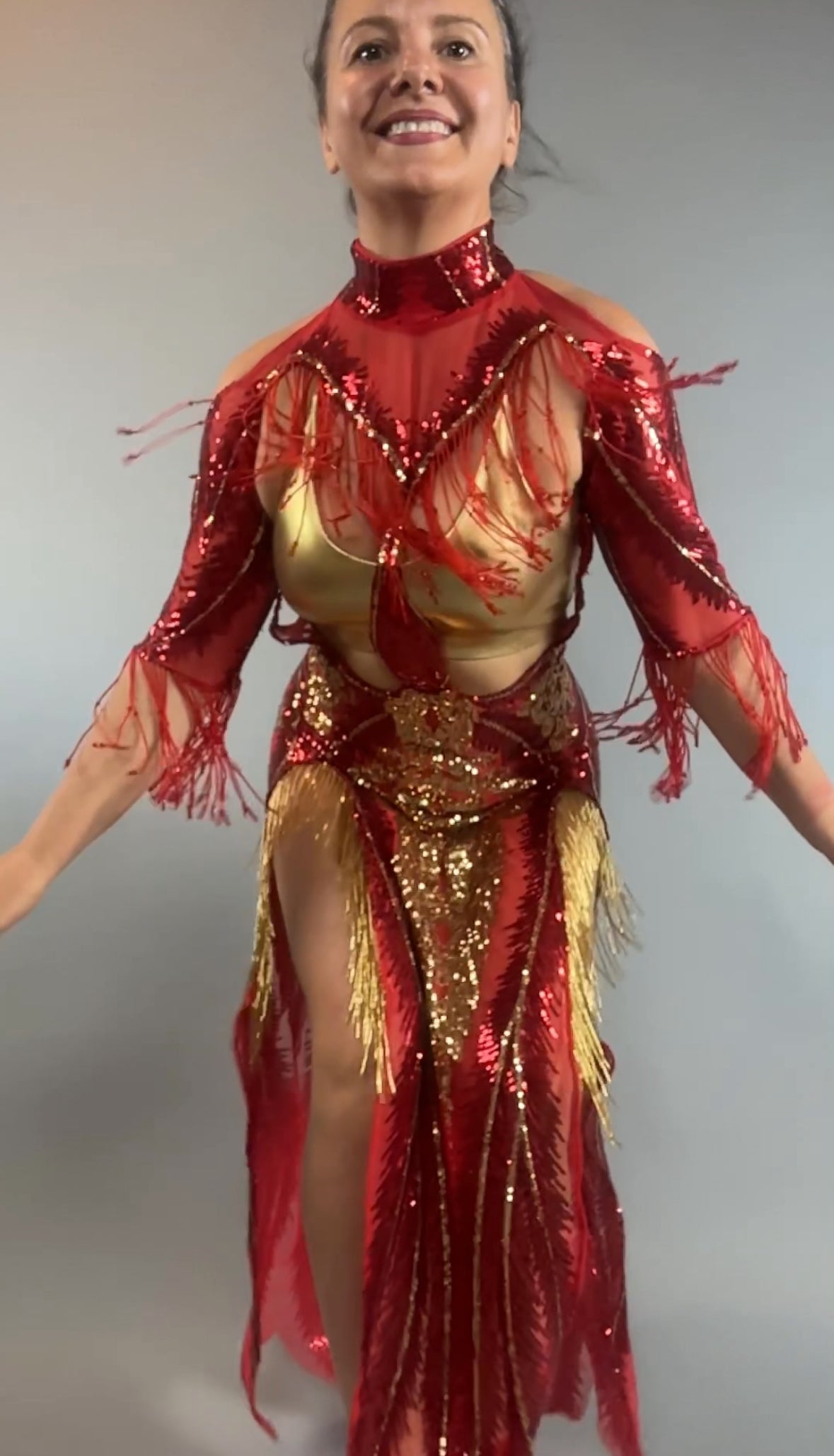 Smiling woman in the bearded French accessories Sequin Sheer Dress, a backless maxi with gold beaded fringe accessories, posing against a plain background.