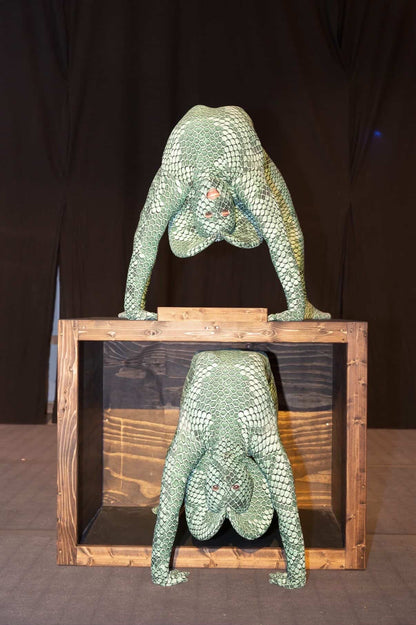 Two performers in Green Pixel Cobra Costumes—snake print catsuits with headdress—pose on and inside a wooden box, their serpent cosplay creating a striking visual against the dark background.