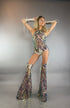 A woman poses in the Chaps pants, laced top, festival costume set adorned with sequins, complete with matching boots and arm wraps, against a plain gray background.