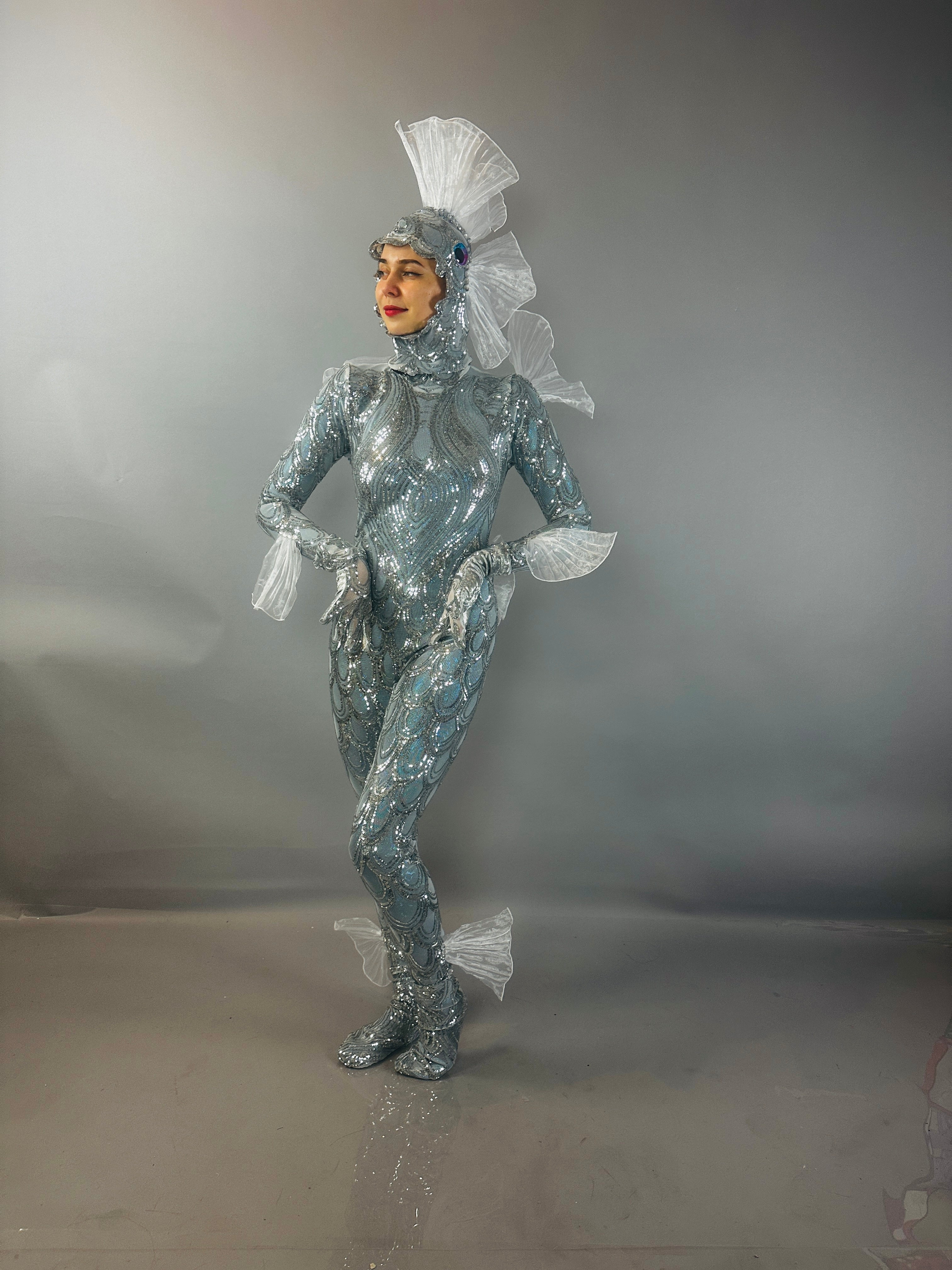 Model wearing the "Sea Creature" costume, featuring shimmering silver fabric and fin-inspired details, highlights couture design against a gray background.