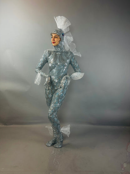 Model wearing the "Sea Creature" costume, featuring shimmering silver fabric and fin-inspired details, highlights couture design against a gray background.