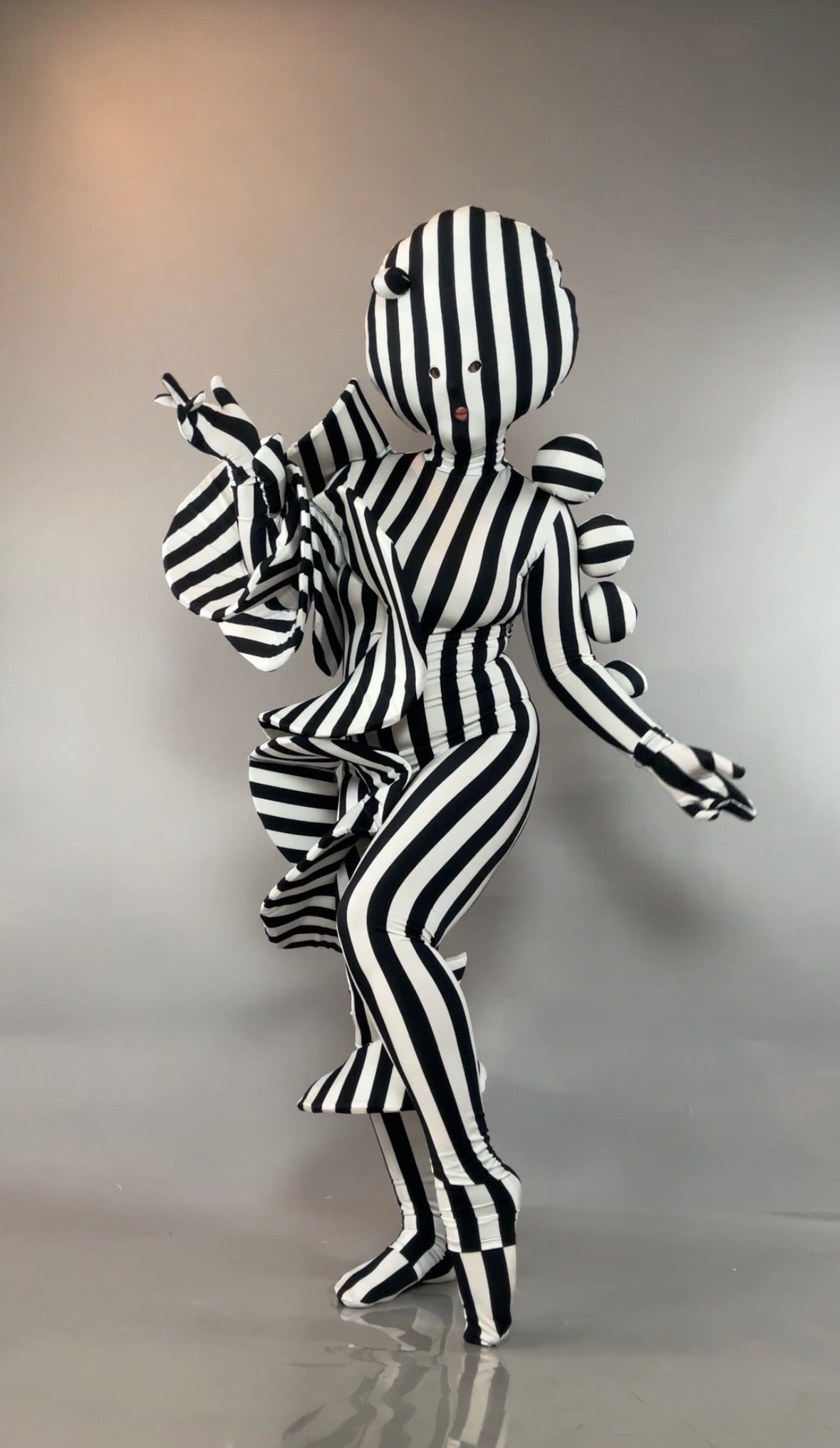 A person in a Black and White Striped Creature Costume with Sculptural Details featuring a round head and ruffles.