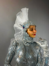 Model wears "Sea Creature": a shiny silver, fish-inspired couture costume with a fin-like headpiece, resembling wearable sculpture against a gray background.