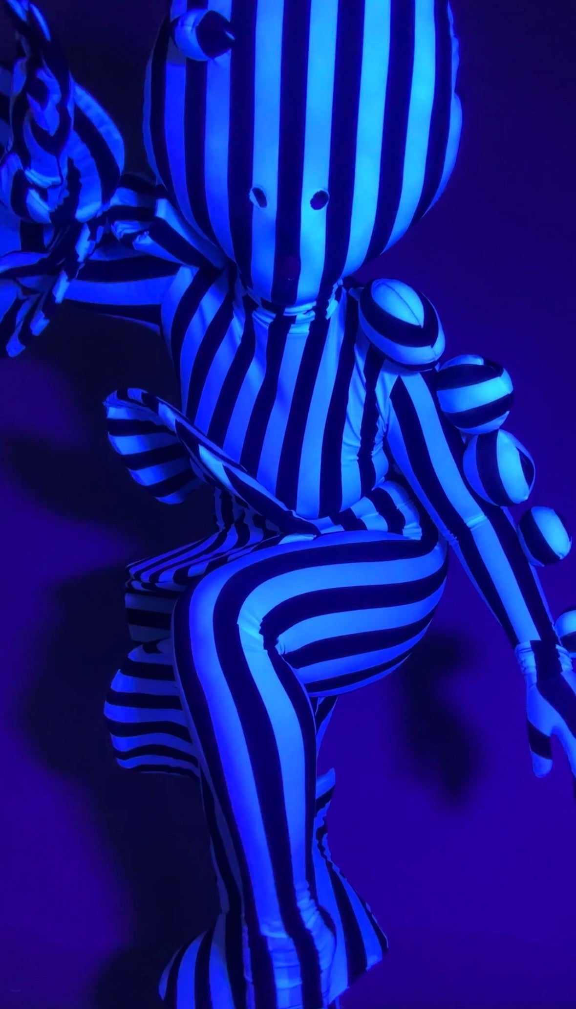 A person in a Black and White Striped Creature Costume with Sculptural Details featuring spherical accents.