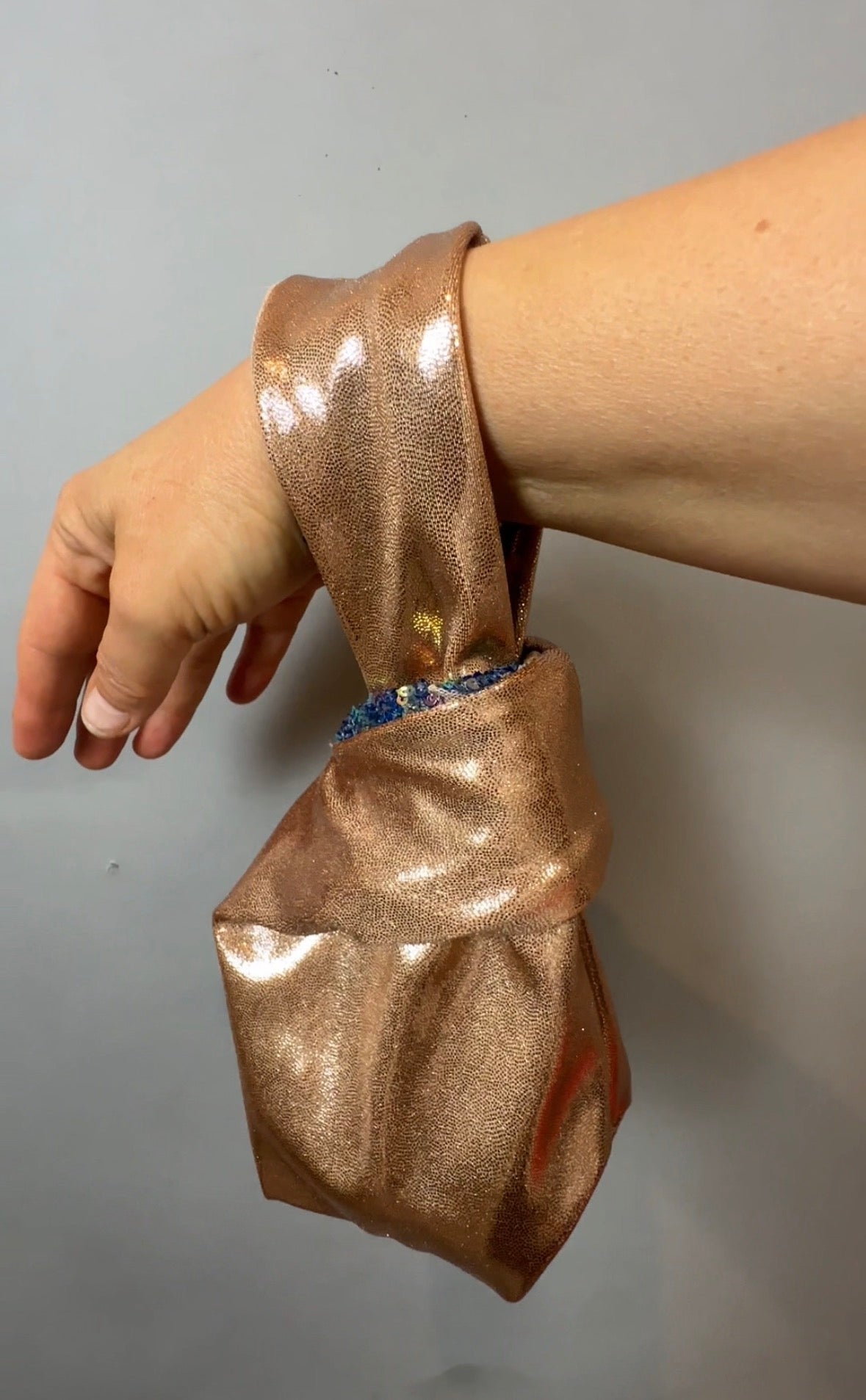 A hand holds a shiny, rose gold, handcrafted reversible sequin mini tote—an elegant, sustainable fashion accessory inspired by Japanese-style bento bags.