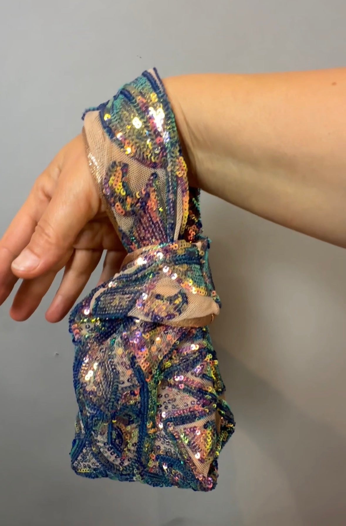 Hand holding a Handcrafted reversible sequin mini tote, a sustainable fashion accessory with wrist strap and Japanese-style closure, against a plain gray background.
