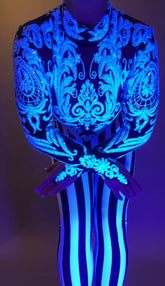 Wearing the Glamorous sequins Stripes Catsuit costume, a person stands with arms crossed, in vivid lighting. The blue and white striped outfit glows with ornate detail.