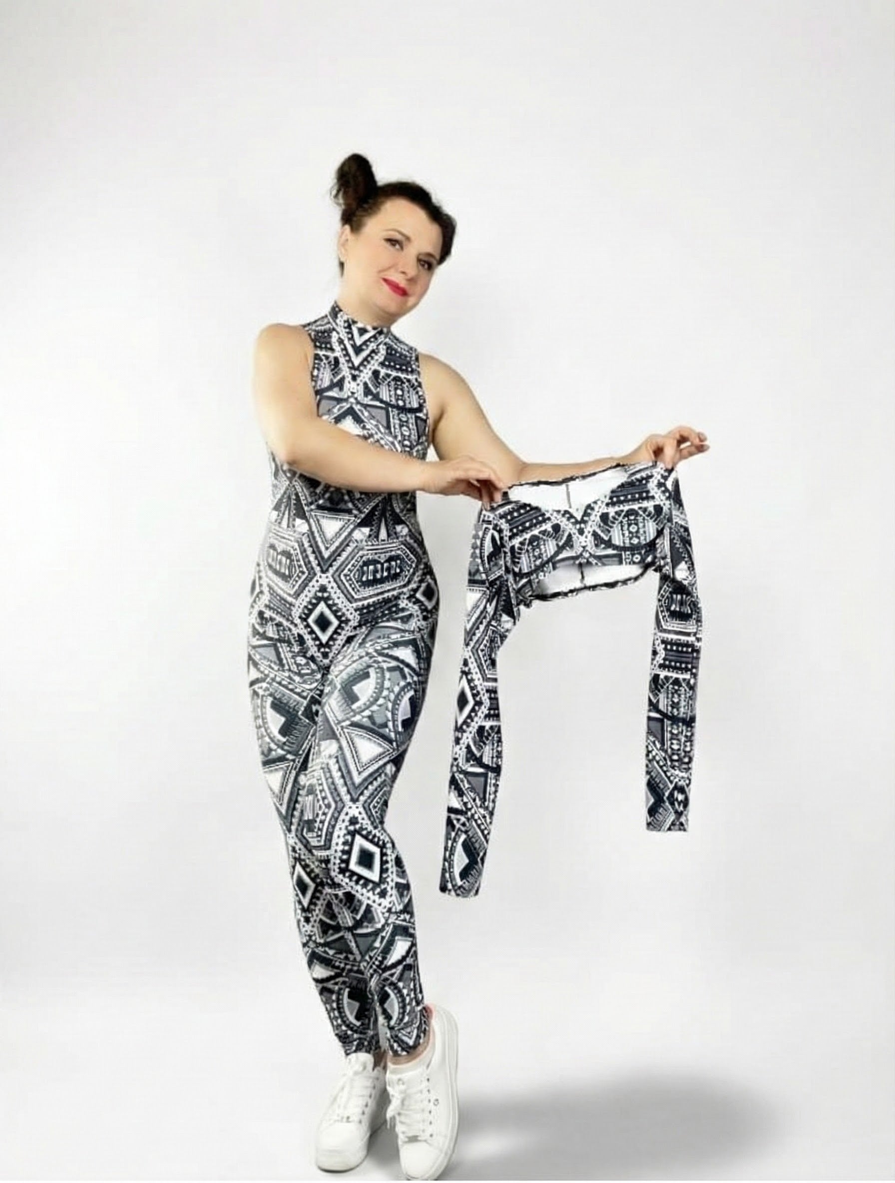 Woman in a black and white UV-reactive tribal print halter neck Geometric Catsuit holds a matching detachable long sleeve shrug against a plain background.