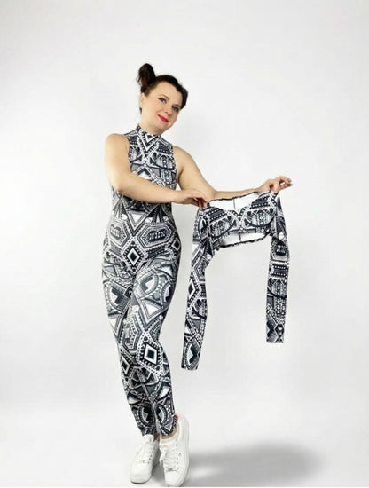 Woman in a black and white UV-reactive tribal print halter neck Geometric Catsuit holds a matching detachable long sleeve shrug against a plain background.