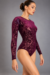 A woman wears a long-sleeve Burgundy Velvet Leotard in burgundy velvet with a floral damask pattern and mesh panels.