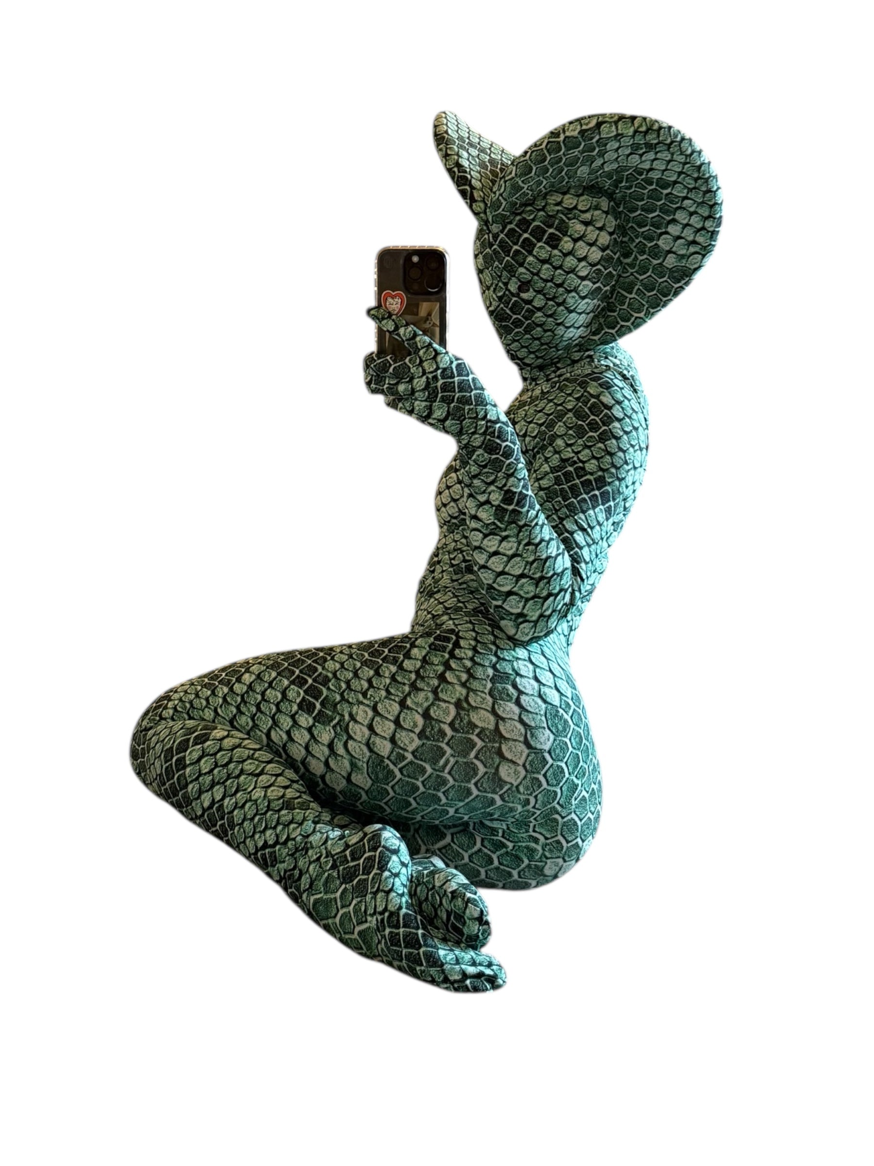 Person wearing the Green pixel Cobra Costume, a snake print catsuit with matching headdress, taking a mirror selfie on their phone.