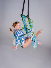Woman wears an Asymmetrical Catsuit for Performers—blue & white porcelain print, one-sleeve, one-leg stretch spandex bodysuit with baroque scroll pattern—posing on a floral hoop against a plain backdrop.