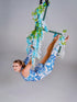 A woman wears the Asymmetrical Catsuit for Performers—a blue & white porcelain print, one-sleeve, one-leg spandex jumpsuit with a baroque scroll pattern—while performing on a floral aerial hoop against a plain background.