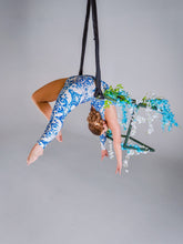 An aerial artist in a blue & white porcelain print asymmetrical catsuit performs suspended upside down on a floral-decorated hoop. The stretch spandex bodysuit features one sleeve, one leg, and a baroque scroll pattern—perfect for dance & events.