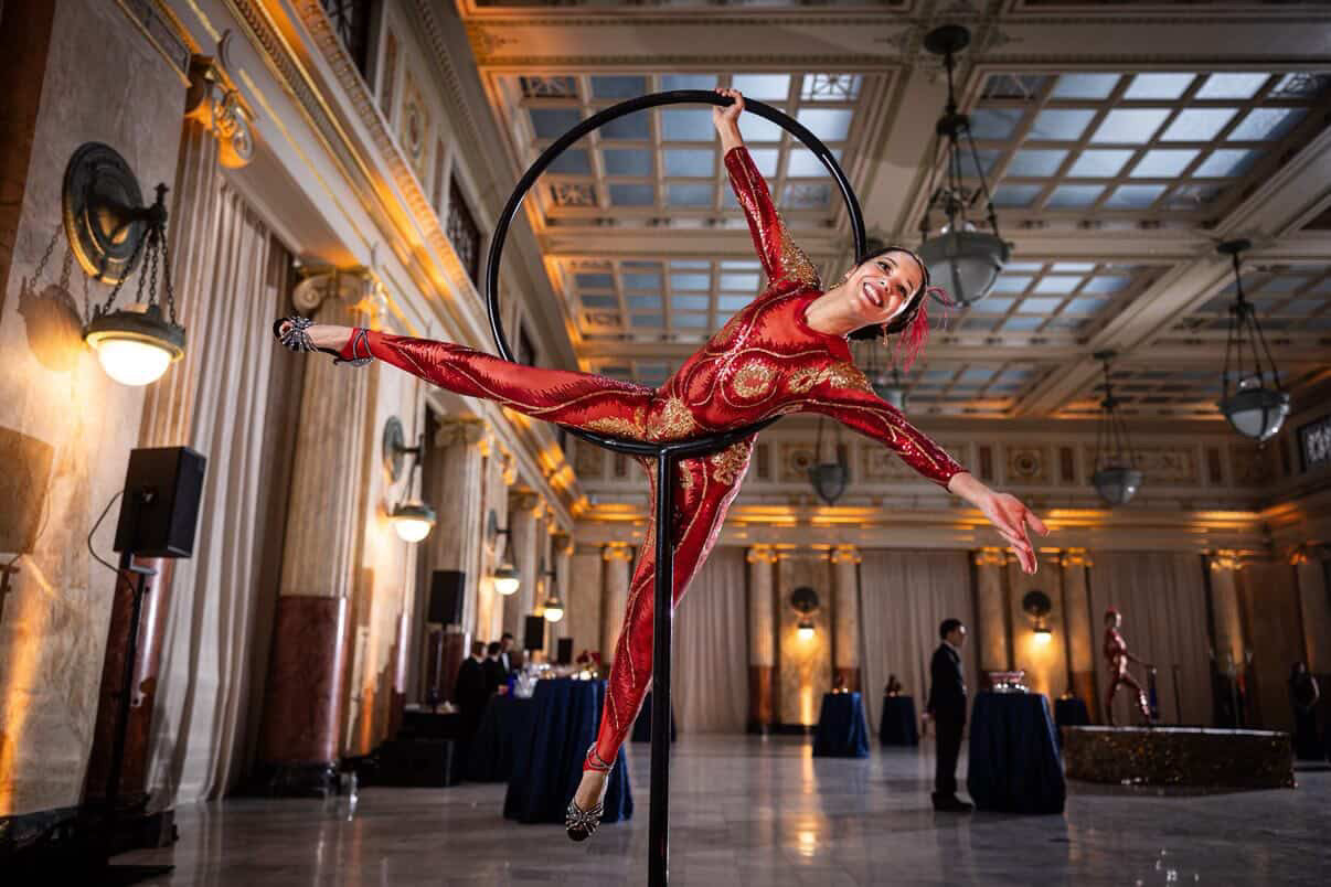 Performer wears the custom-made Showgirl Costume—Sequin Bodysuit for Women or Men, a black sheer jumpsuit perfect for bellydance or bridal looks—posing on a hoop in an elegant hall with high ceilings and chandeliers.