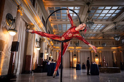 Performer wears the custom-made Showgirl Costume—Sequin Bodysuit for Women or Men, a black sheer jumpsuit perfect for bellydance or bridal looks—posing on a hoop in an elegant hall with high ceilings and chandeliers.