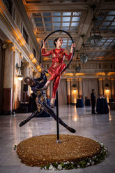 Two acrobats perform on a hoop in an elegant hall, wearing custom-made Showgirl Costumes: black sequin bodysuits with sheer details, designed for both women and men.