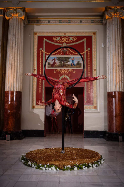 An acrobat in a custom-made black sequin bodysuit performs an upside-down split on a hoop in an ornate hall, wearing the Showgirl Costume, Sequin Bodysuit for Women or Men.