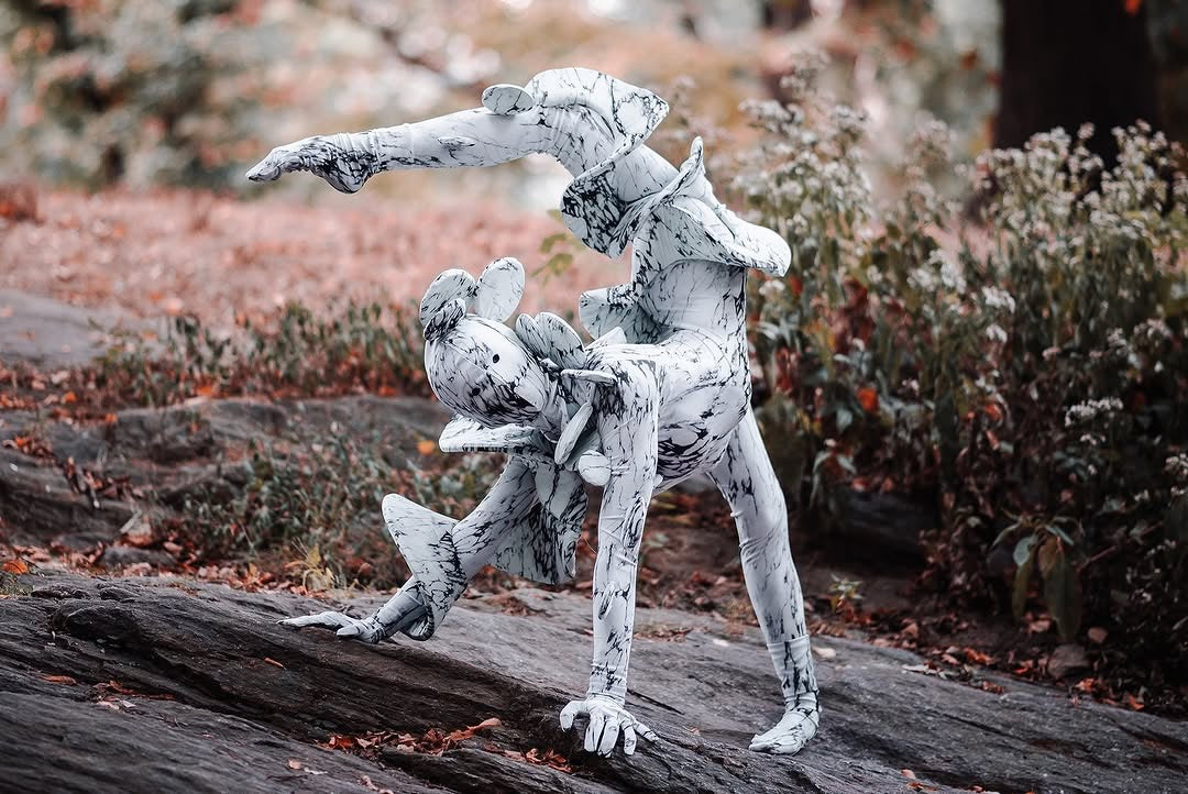 Two people wear matching Mushroom fungus Costumes, striking a balancing pose on rocks in a forest—futuristic fashion and exotic dance wear perfect for Burning Men and trending artistic performances.