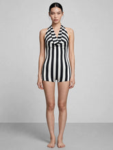 A woman stands barefoot against a gray background, wearing the Black and White Striped Leotard featuring a halter top with an open back.