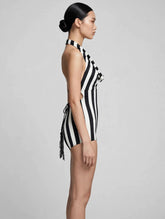 A woman in a black and white striped leotard with a halter top and open back stands in profile against a plain background.