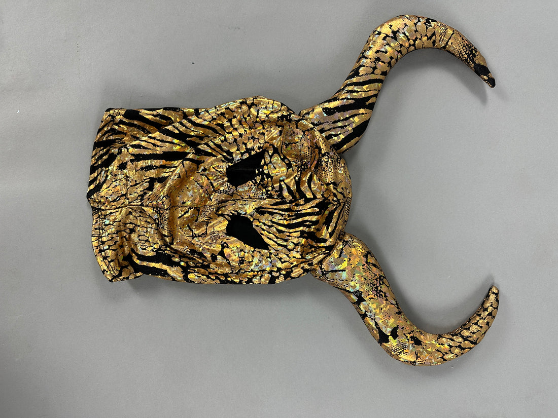 The Gold & Black Gazelle Creature Costume features a mask with elegantly curved horns, reminiscent of a gazelle headdress against a gray backdrop.