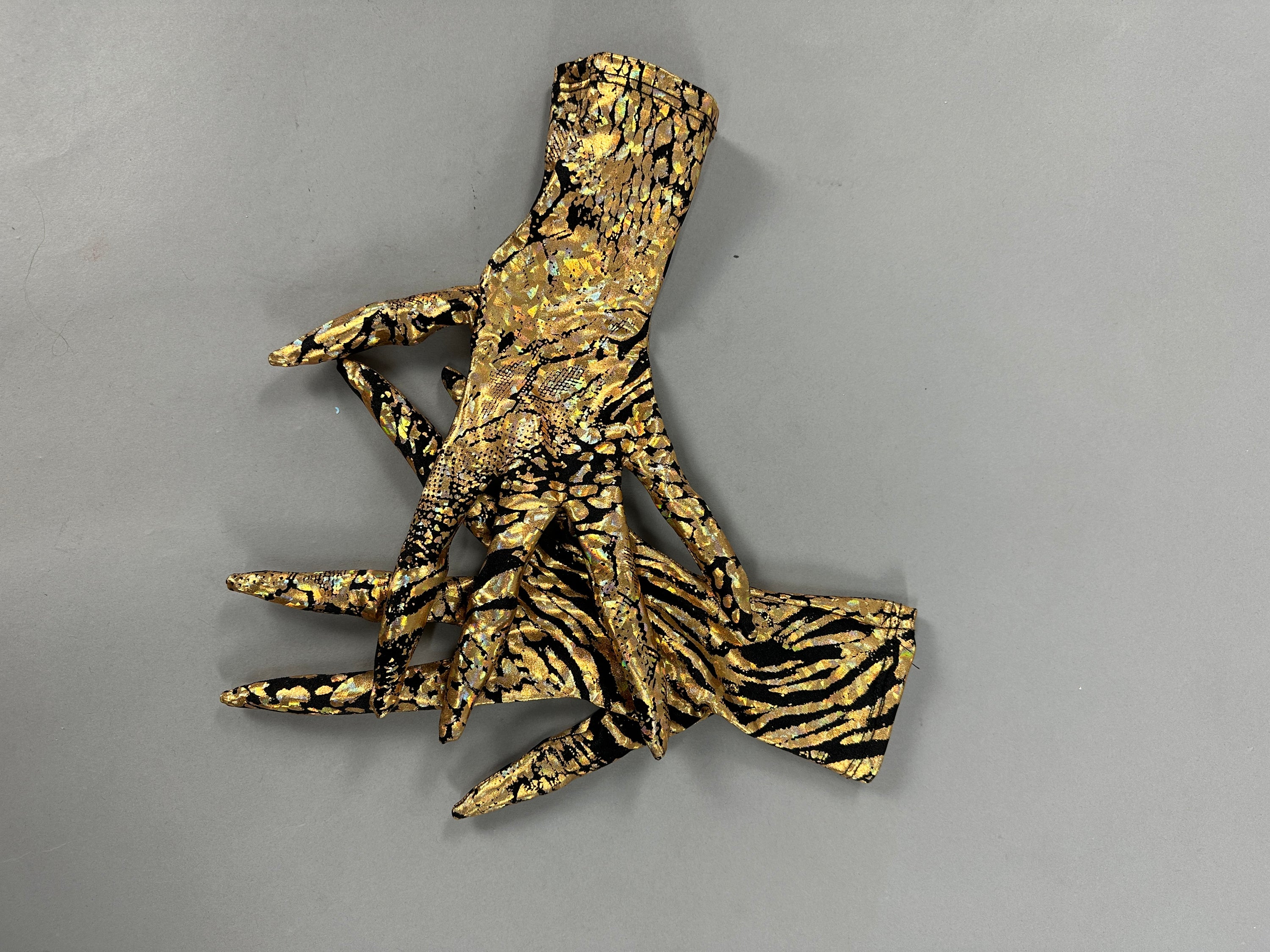 A metallic gold and black hand sculpture with abstract designs on a gray background resembles the Gold &amp; Black Gazelle Creature Costume, featuring a full sleeve catsuit, headdress, gloves, and socks.