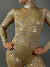 Model strikes a pose with hands on hips in the Champagne Fairy Sequin Catsuit featuring an open back, turtleneck, and sleeves, set against a gray background.