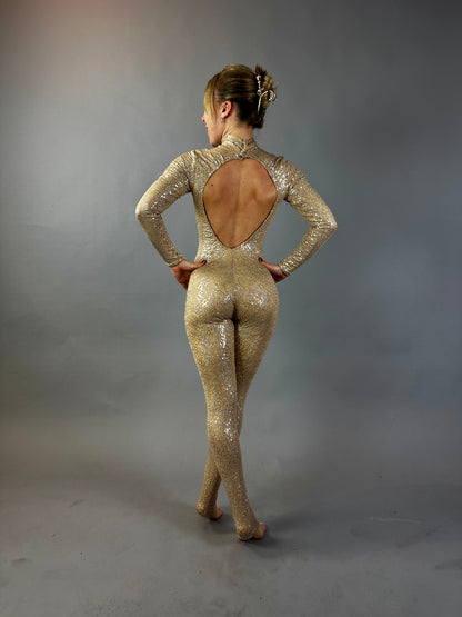 A woman in a Champagne Fairy Sequin Catsuit with an open back and turtleneck stands in a studio with a gray backdrop, the sparkly performance costume&