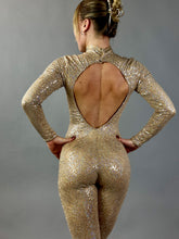 A woman wearing the Champagne Fairy Sequin Catsuit—an open-back, turtleneck jumpsuit with sleeves—stands against a plain gray background.