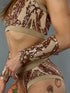 Wearing the Sequin Crop Top and Bottom Set, a person in a shimmering gold halter neck crop top, shorts, and patterned dance outfit showcases leg tattoos against a neutral backdrop. This dazzling performance wear captures the spotlight with ease.