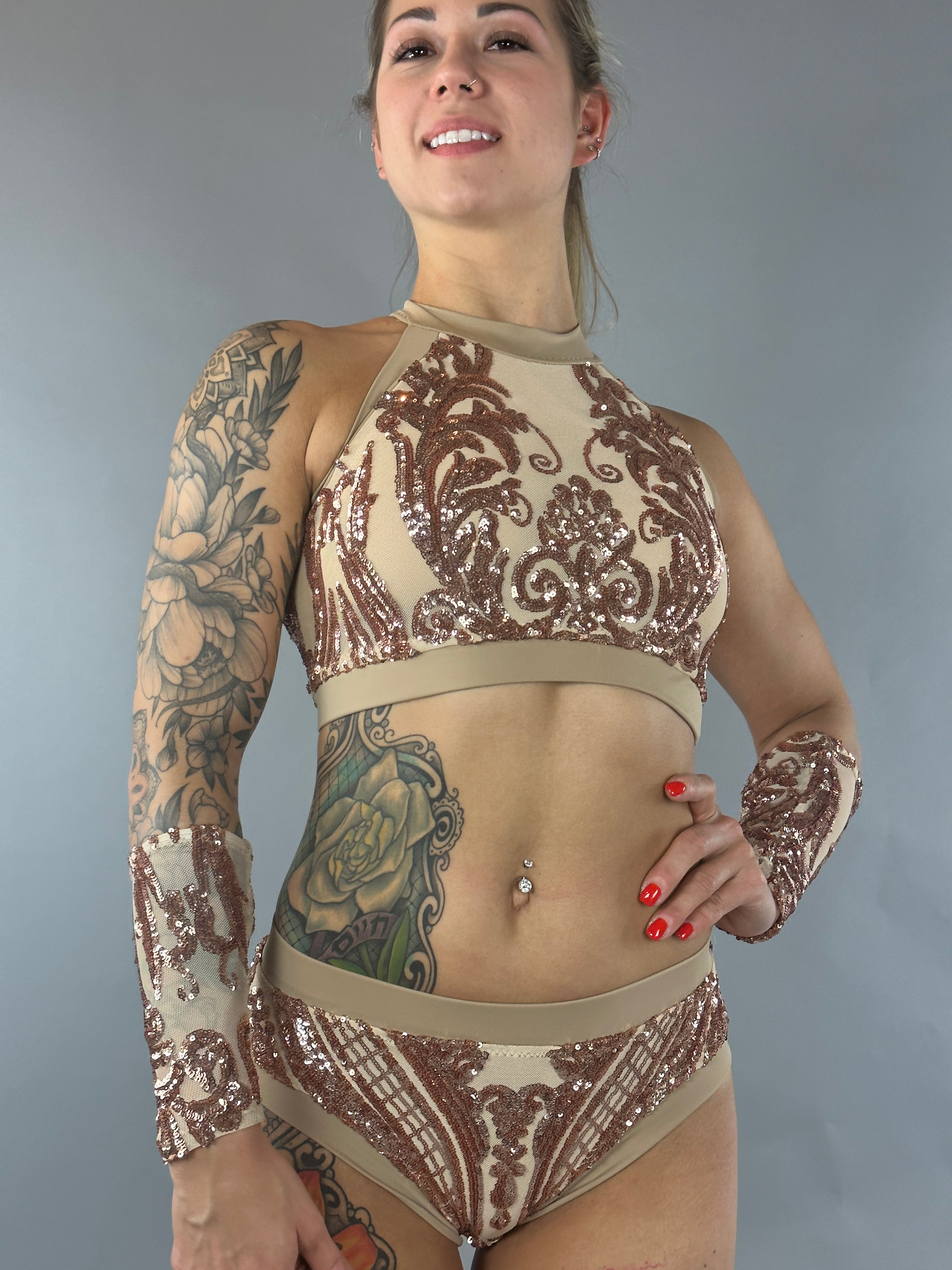 Wearing a shimmering Sequin Crop Top and Bottom Set, the person smiles confidently against a neutral backdrop, the halter neck crop top perfectly complementing their tattoos.
