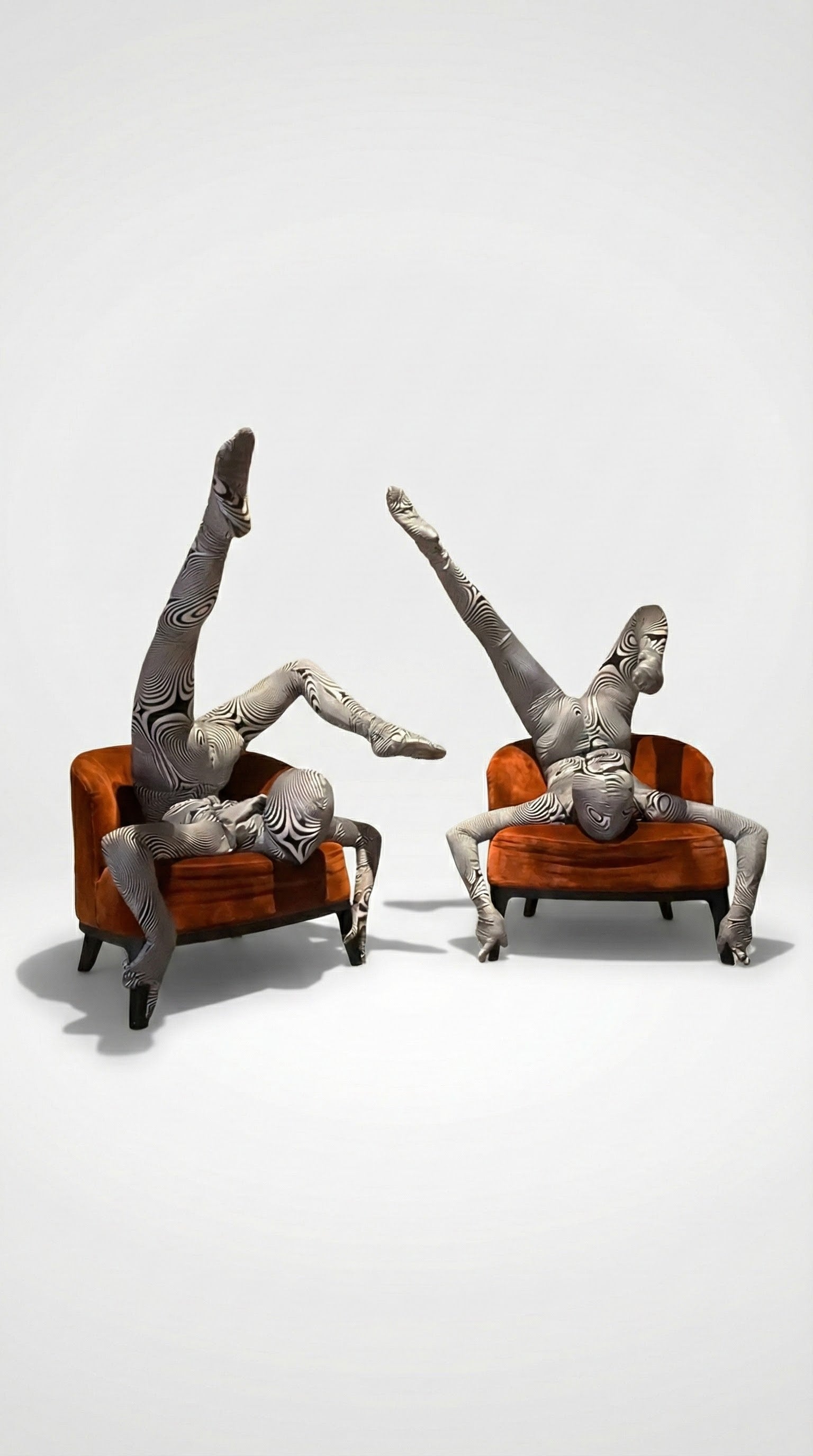 Two people in patterned bodysuits perform acrobatic poses on orange chairs against a plain background, showcasing the Alien Costume—futuristic fashion that&