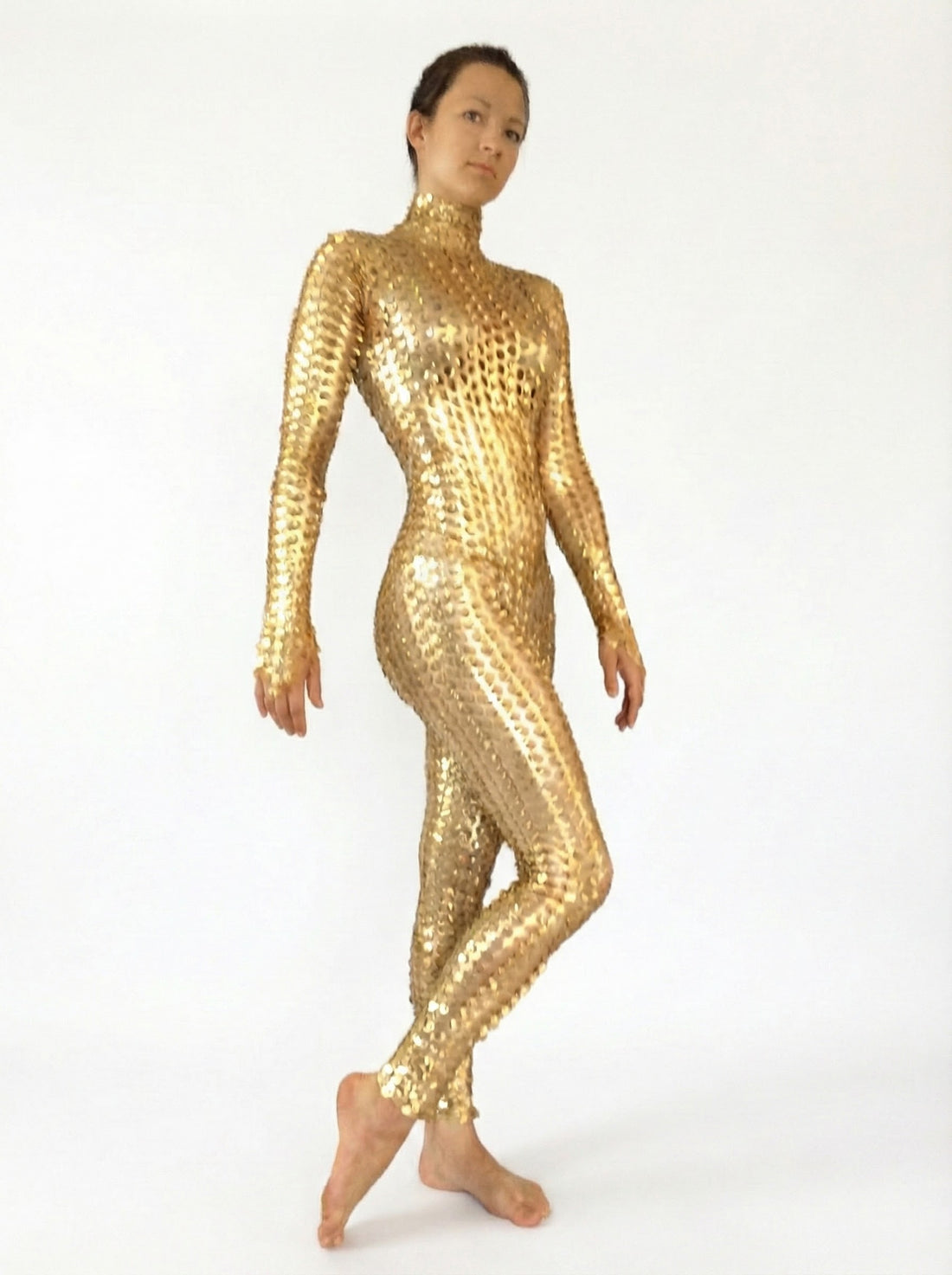 A person poses barefoot in the Metallic Gold Spiky Catsuit, a shiny, form-fitting full body spandex jumpsuit with 3D texture and futuristic robot style, against a plain white background.