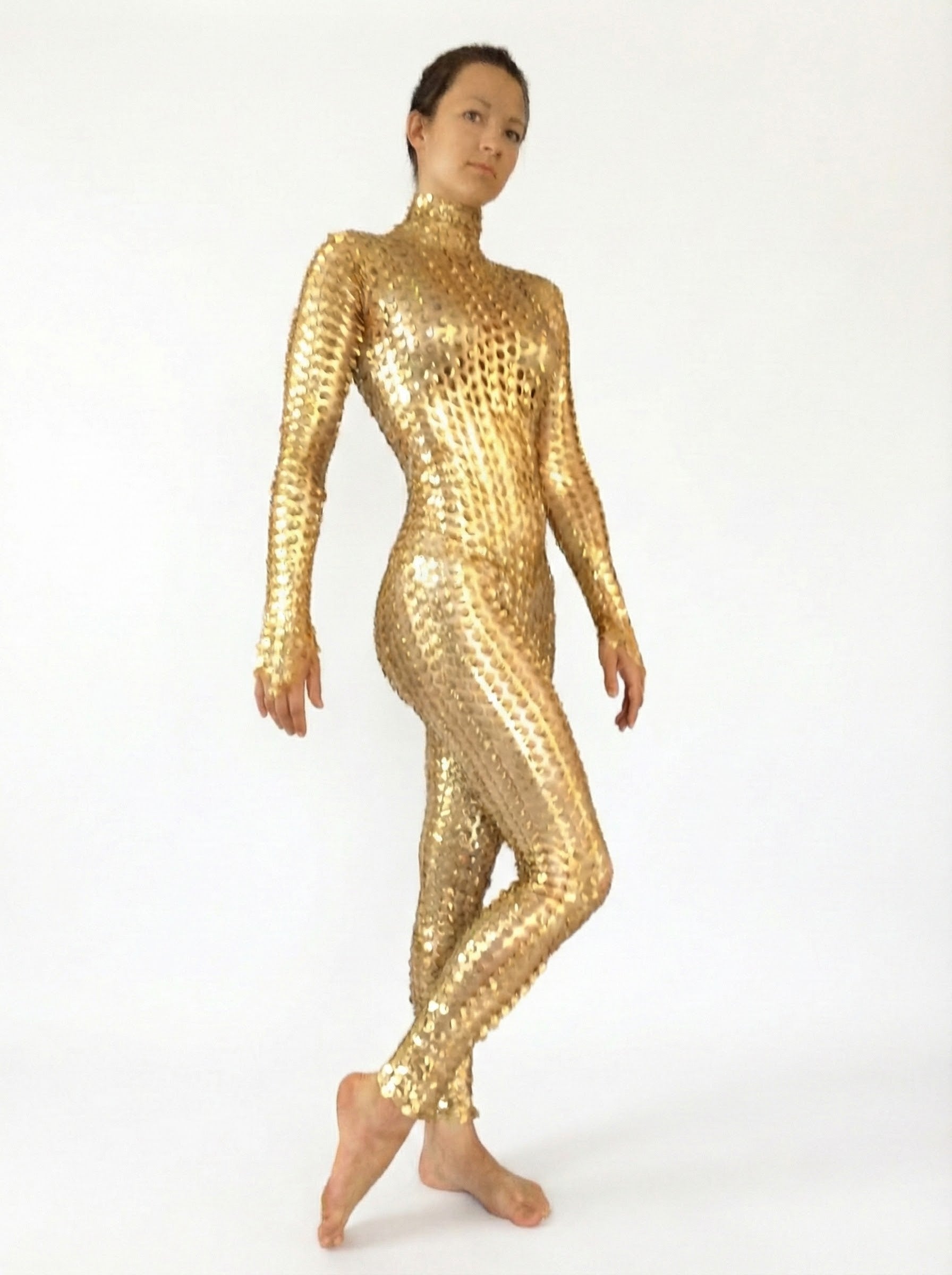 A person poses barefoot in the Metallic Gold Spiky Catsuit, a shiny, form-fitting full body spandex jumpsuit with 3D texture and futuristic robot style, against a plain white background.
