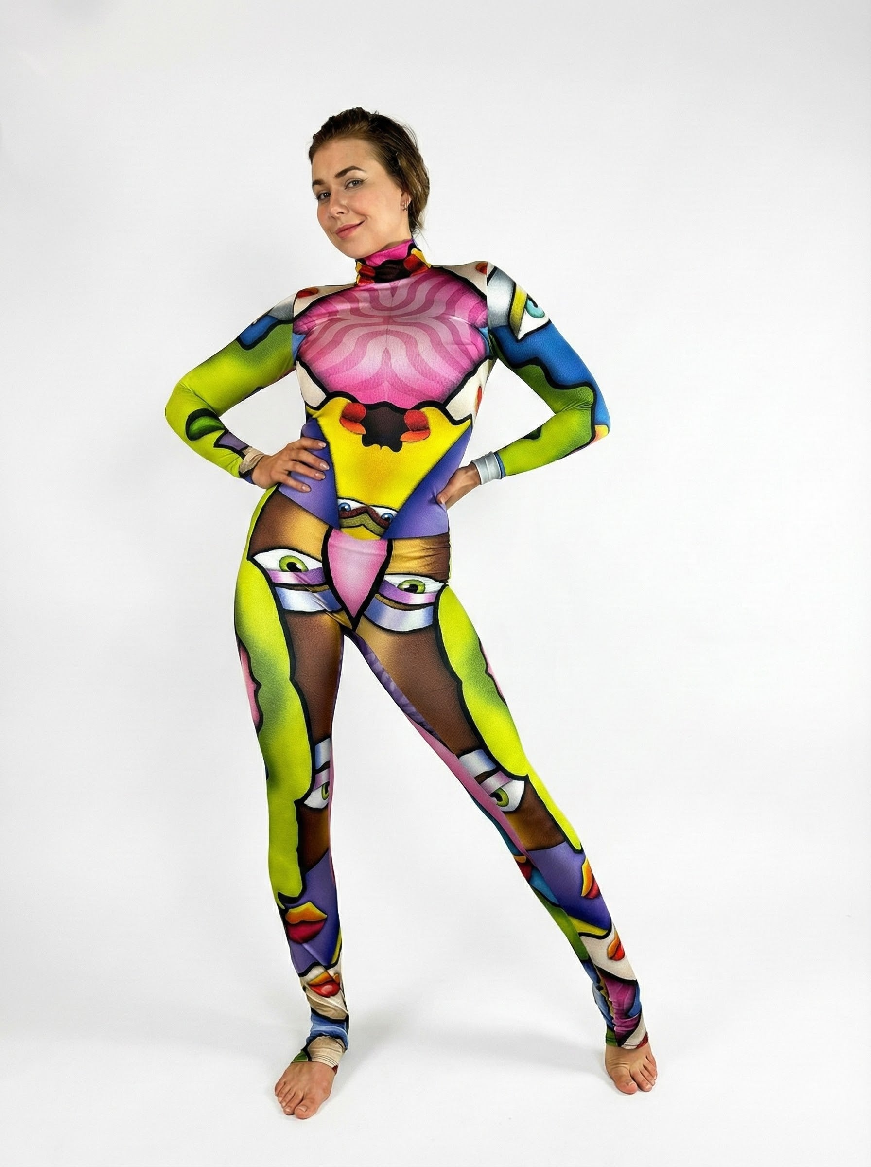 Model wears the Multicolor Picasso Catsuit featuring a turtleneck, long sleeves, and vibrant face-like abstract patterns, posed against a white background.