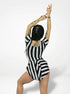 Wearing the Striped Leotard With Skirt, this person poses with arms raised, displaying tattoos and braided hair—perfect for dance teachers, aerialists, gymnasts, or fire performers seeking trending exotic dancewear.